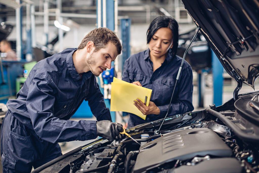 Auto Car Repair Service Center. Two Mechanics   Man And Woman Examining Car Engine